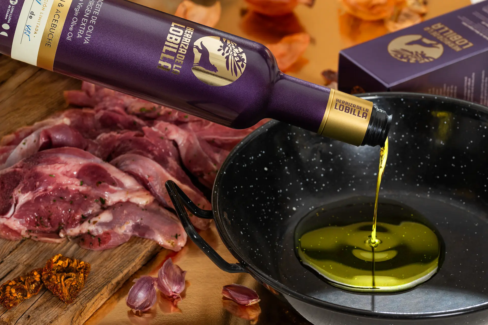 Botella de aceite de oliva virgen extra variedad lechín y acebuche vertiendo el producto sobre una sartén con una tabla de carne macerada al fondo