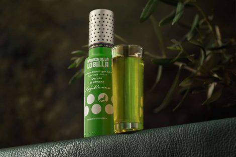 Botella pequeña de aceite de oliva virgen extra variedad hojiblanca con un vaso alargado mostrando el producto y su color característico