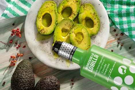 Botella de aceite de oliva virgen extra variedad hojiblanca aplicando el producto sobre plato con aguacates en su punto perfecto de maduración