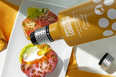 Estuche regalo Hojiblanca + Picual 16 Botella de aceite de oliva virgen extra variedad envero vertiendo el producto sobre tomates cortados