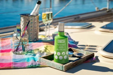 Botella de aceite de oliva virgen extra variedad hojiblanca en composición tipo bodegon con fondo de piscina de hotel, cubertería y botella y copas de cava